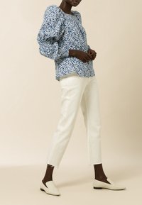 Bluse med puffede ærmer i blåt og hvidt blomstermønster, kombineret med hvide bukser med lige ben og lyse loafers.