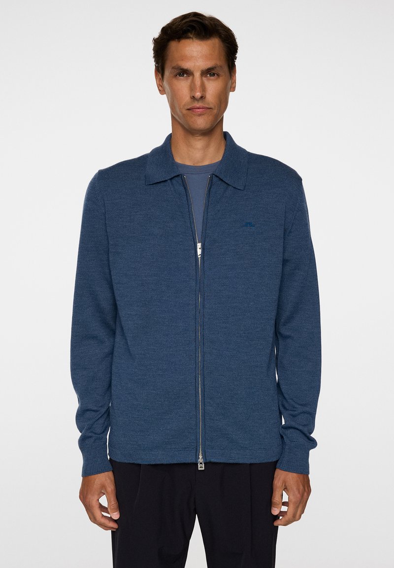 Cardigan blu con zip realizzato in morbido tessuto a maglia, caratterizzato da un colletto piatto, maniche lunghe e un discreto dettaglio del logo sul petto.