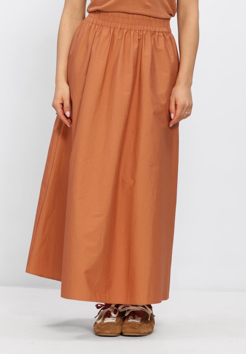 Woman wearing a rust-colored ankle-length skirt with an elastic waistband and brown moccasin-style shoes with laces.
