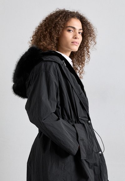 Black outerwear featuring a fur-lined hood, drawstring waist, button closure, and textured fabric, designed for warmth and comfort.