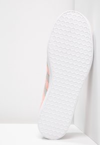 Růžové a šedé tenisky s texturovanou bílou gumovou podešví. Mají měkký textilní svršek se třemi šikmými šedými pruhy.