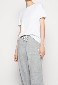 Bílý bavlněný tričko s krátkým rukávem spárované se šedými tepláky s tkaničkou a jemnou strukturou. Na teplácích je logo Nike.