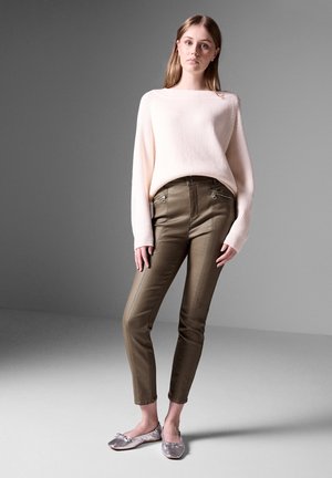 Maglione rosa chiaro a coste con un ampio scollo, abbinato a pantaloni verde oliva slim-fit con tasche zip e ballerine grigio chiaro con fiocchi.