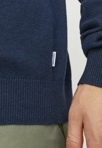 Maglione lavorato a maglia blu navy con polsini e orlo a coste, presenta un piccolo etichetta bianca con la scritta "JACK & JONES" sul lato.