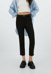 Černé kalhoty na míru se slim fit střihem a zkrácenou délkou, spárované s světle modrou košili a silnými černými mokasíny. Opasek součástí.