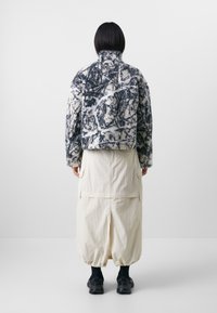 Fuzzy, cropped jacket with a black and white abstract pattern, paired with a beige skirt featuring pockets and a drawstring hem.