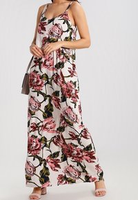 Maxiklänning med blommönster i rosa och grönt på en krämfärgad bakgrund, med tunna axelremmar och ett flödande, lätt tyg.