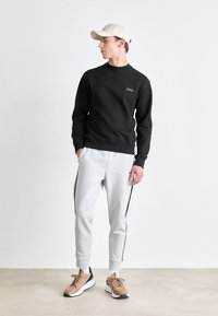 Black sweatshirt with a round neckline, paired with light gray joggers featuring black side stripes. Light-colored cap and tan sneakers.
