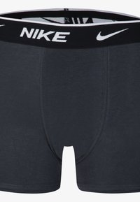 Temno sivi bokserice iz mehkega materiala, s črnim pasom in belim logotipom "NIKE" ter detajli šivanja.