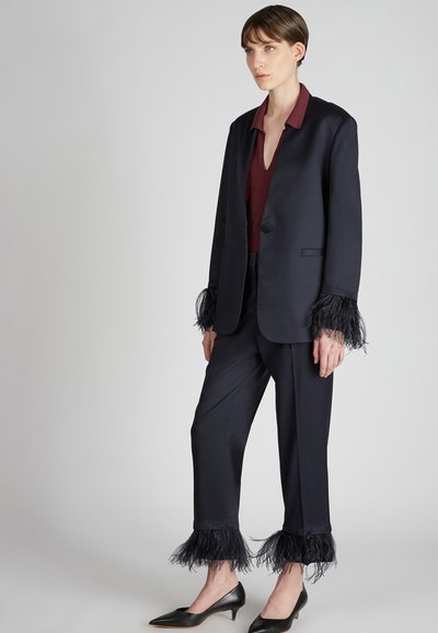 Marynarski blezer z piórowymi akcentami na mankietach, w zestawieniu z pasującymi spodniami. Bordowy top pod spodem z dekoltem w kształcie litery V. Czarne szpilki.