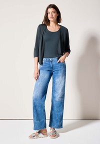 Un cardigan gris foncé sur un débardeur sombre, associé à un jean large bleu clair et des sandales argentées. Textures douces et coupe décontractée.