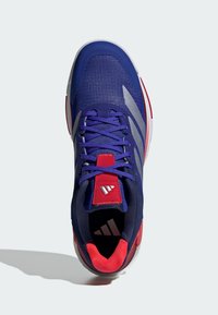 Sport shoes featuring a blue mesh upper with red and gray accents, round toe, and a textured sole. Includes purple laces and logo on the tongue.
