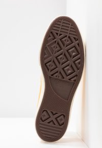 Semelle en caoutchouc marron d'une basket Converse All Star montrant les motifs de la semelle et le logo de la marque sur un fond clair.