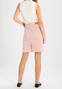 Rosa denimkjol med slits bak, medellång, hög midja design, med en kontrasterande brunt lädermärke i midjan.