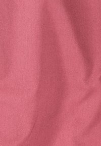 Nahaufnahme von rosa strukturiertem Stoff mit diagonalem Webmuster und dezenten Schatten, die sanfte Falten betonen.