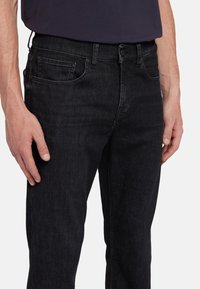 Jeans in denim nero con vestibilità dritta, dotati di tasca frontale e cuciture a contrasto sottili. Texture liscia con una leggera lucentezza.