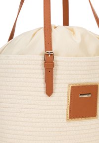 Beige geweven tas met een trekkoordsluiting, roomkleurige voering en bruine leren accenten. Voorzien van een gouden logo plaat.