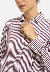 Button-up shirt in white and burgundy stripes, featuring a collar, long sleeves, and small buttons along the front placket.