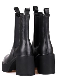Botas de mujer de cuero negro hasta el tobillo con paneles laterales elásticos, punta redondeada y tacón cuadrado grueso. Textura suave y líneas limpias.