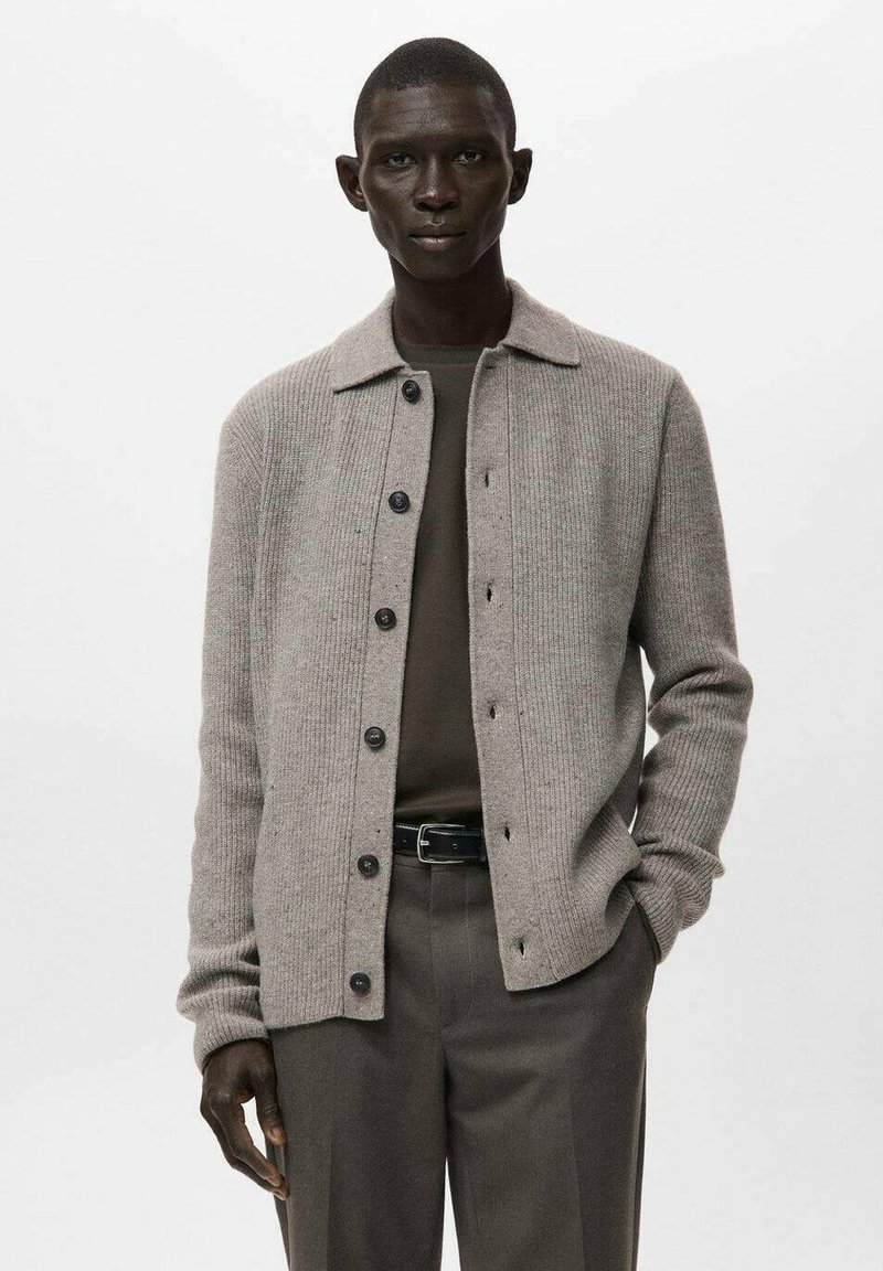 Szary prążkowany kardigan z kołnierzykiem, zapinany na guziki z przodu, z długimi rękawami. Noszony na ciemnozielonej koszuli, w połączeniu z dopasowanymi spodniami.
