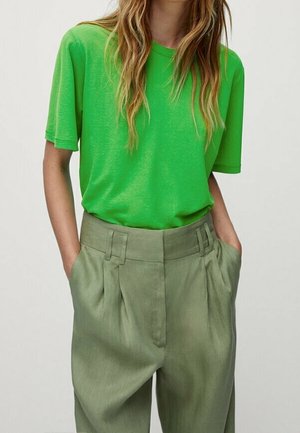 Woman wearing bright green short-sleeve t-shirt tucked into high-waisted, loose-fitting olive green pants with hands in pockets.