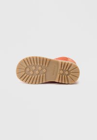 Sola de sapato laranja com uma superfície de borracha texturizada, apresentando um padrão de ranhura para aderência e a marca "WHEAT" perto do calcanhar.