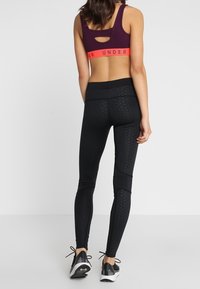 Czarne legginsy z teksturowanego materiału z siateczkowymi wstawkami, zestawione z bordowym stanikiem sportowym z wycięciem i jasną elastyczną taśmą.