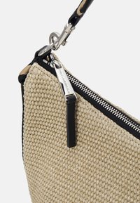Coin d'une pochette tissée beige avec fermeture éclair argentée, bord en tissu noir et fermoir métallique fixé à une sangle noire.