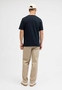 Zwarte T-shirt met korte mouwen en ronde hals, gecombineerd met beige broeken en witte sneakers. Achteraanzicht, minimalistisch ontwerp, zonder patronen.
