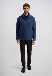 Blauer, strukturierter Pullover mit Reißverschlusskragen, kombiniert mit dunklen Hosen und polierten Schuhen, alles vor einem schlichten Hintergrund.