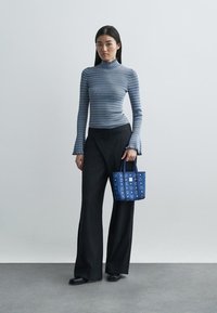 Un col roulé rayé bleu, un pantalon large à rayures noires, et un petit sac fourre-tout à motif bleu avec une poignée. Textures lisses, coupe ajustée.