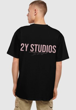 Black cotton t-shirt featuring "2Y STUDIOS" in pink text on the back, casual fit, short sleeves, with a smooth texture.