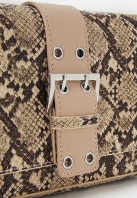 Taška s texturou hadí kůže a koženým páskem v barvě tan, vybavená stříbrným kováním, dvěma otvory ve stylu průvleku a dekorativní sponou.