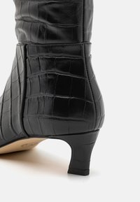 Bottines en cuir noir avec une texture embossée crocodile, un talon fin et un bout arrondi. Détails de couture sur le côté visibles.