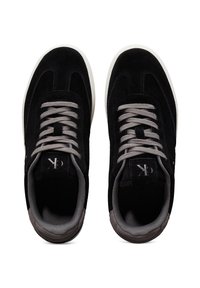 Schwarze Wildledersneaker mit grauen Schnürsenkeln, die eine glatte Textur, eine abgerundete Form und weiße Gummisohlen aufweisen. Akzente sind ein Logo auf der Zunge.