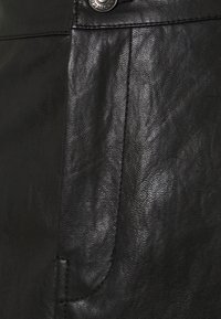 Lähellä oleva musta nahkakangas, jossa on sileä pinta, hienovarainen kiilto ja näkyvät tikkaustyöt taskun ja napin yksityiskohdissa.