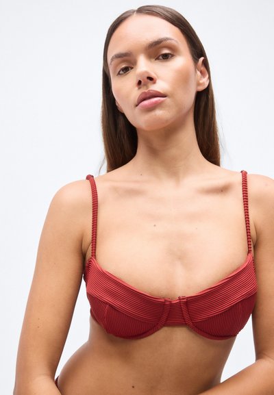 Κόκκινο μπικίνι τοπ με ριμπ ύφανση, λεπτές υφασμάτινες τιράντες και σχεδιασμό με δομημένα cups. Κατακόρυφες γραμμές προσδίδουν οπτικό ενδιαφέρον. Δεν φαίνονται μεταλλικά μέρη.