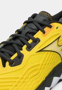 Baskets de course jaunes avec une tige en mesh texturé, lacets noirs et accents synthétiques. Coutures en zigzag remarquables le long du col.