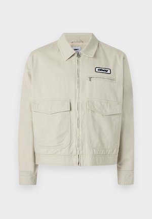 Smėlio spalvos džinso striukė su užtrauktuku, dviem priekinėmis kišenėmis ir mažu logotipu. Struktūruotas dizainas su apykakle ir ilgomis rankovėmis.