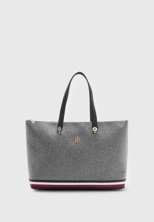Bolsa tote gris con asas negras, emblema de logo dorado y ribete a rayas rojas, blancas y negras en la parte inferior sobre un fondo blanco.