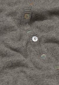 Graue Strickjacke mit großen, runden, schimmernden Knöpfen. Der Stoff hat eine weiche Textur mit einem leicht gerippten Muster entlang der Knopfleiste.