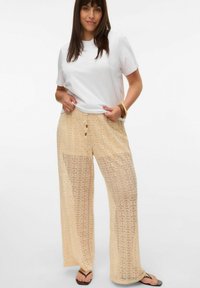 Beige blonde bukser med løs pasform, der har snøring i taljen og indviklede cirkulære mønstre, parret med en simpel hvid t-shirt.