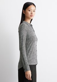 Schwarz-weißer gemusterter Langarmhemd mit durchgehender Knopfleiste und Kragen, glatter Textur und taillierter Silhouette.