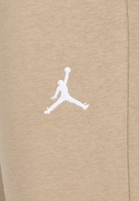 Tissu en jersey beige avec un logo Jumpman brodé blanc, présentant une texture lisse et un design athlétique, positionné sur le côté gauche.