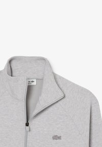 Giacca zip grigia con colletto alto, realizzata in tessuto testurizzato. Presenta un logo sul lato sinistro del petto e un design dal fitting classico.