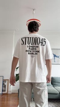 Bijela pamučna majica s podebljanim crnim natpisom na leđima: "STUDIO45 LONDON PARIS NEW YORK BERLIN." Kratki rukavi, opušteni kroj.