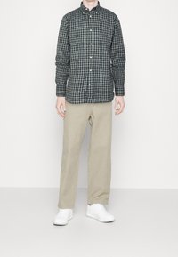 Camisa de cuadros verde y azul marino de botonadura, con mangas largas, combinada con pantalones beige y zapatillas blancas.