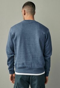 Felpa blu scuro con polsini e orlo a coste. Realizzata in un tessuto morbido, presenta un classico scollo rotondo e una vestibilità comoda.