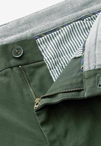 Groene katoenen broek met een rits- en knoopsluiting. De binnenkant heeft een gestreepte voering met een grijze tailleband en kleurrijke accentdetails.