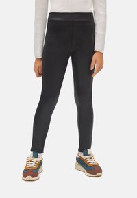 Leggings negras con una textura suave, diseño de cintura alta, complementadas con zapatillas de estilo retro coloridas con paneles en contraste.